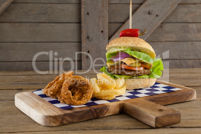 Hamburger, onion ring and french fries on chopping board