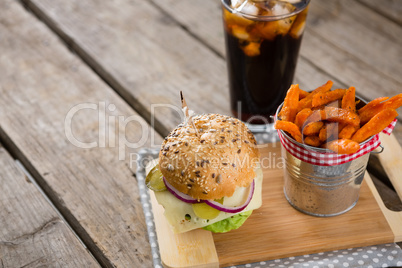 French fries in container by burger on cutting board with drink