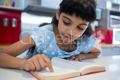 Close-up of girl pointing while reading novel in kitchen