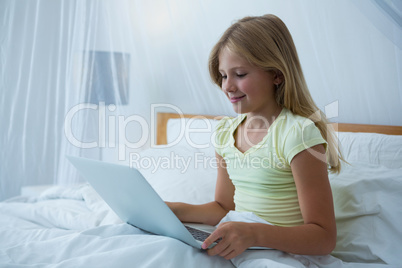 Girl using laptop while sitting on bed
