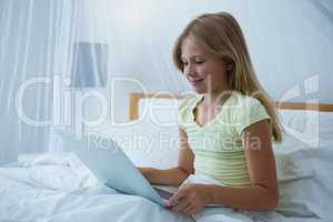 Girl using laptop while sitting on bed