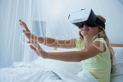 Girl using virtual reality simulator while sitting on bed