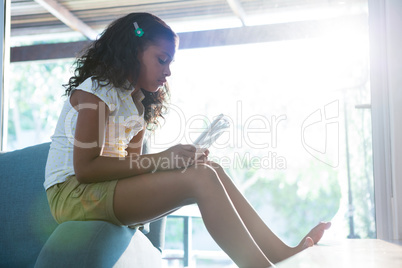 Side view of girl using tablet while sitting on armchair