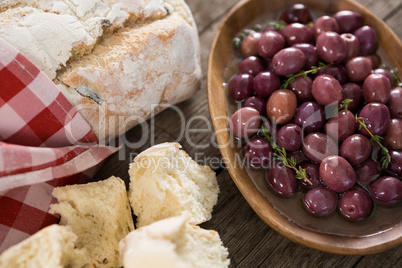 Marinated olives with bread loaf on wooden table