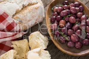 Marinated olives with bread loaf on wooden table