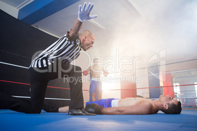 Referee gesturing by unconscious male boxer lying in ring