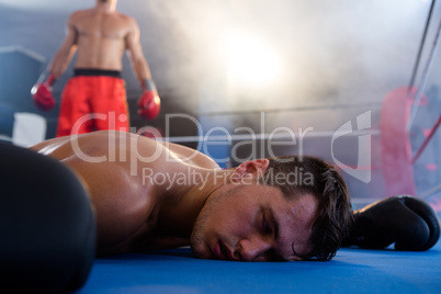 Unconscious male boxer lying by athlete in ring