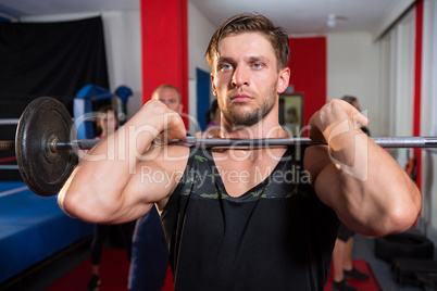 Young male athlete lifting barbell by boxing ring