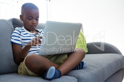 Boy using laptop while sitting with crossed legged on sofa at home