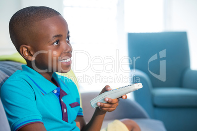 Smiling boy holding remote control on sofa at home