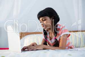 Girl typing on laptop while lying in bedroom
