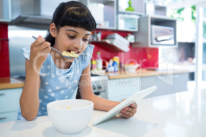 Girl eating breakfast while looking at digital tablet