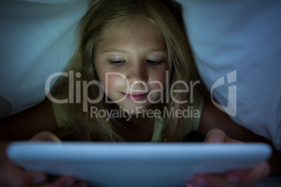 Girl using tablet computer under blanket