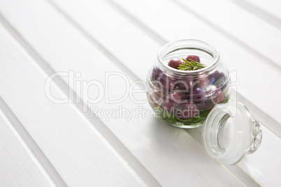 Marinated olives with herbs in a glass jar on table