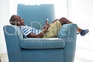 Portrait of smiling boy with mobile phone while lying on armchair at home