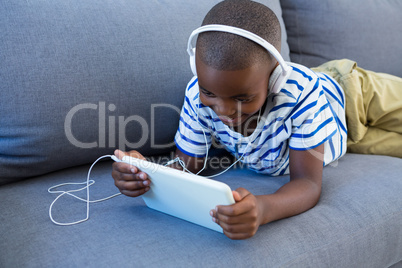 Smiling boy using digital tablet while listening to headphones on sofa at home