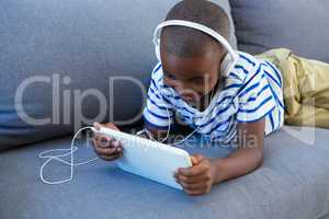 Smiling boy using digital tablet while listening to headphones on sofa at home