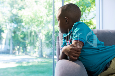 Thoughtful boy looking through window at home