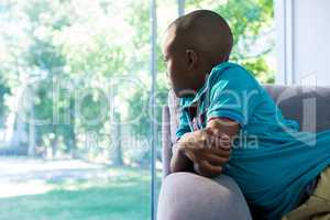 Thoughtful boy looking through window at home