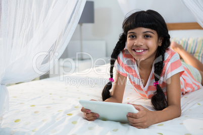 Smiling girl using digital tablet on bed at home