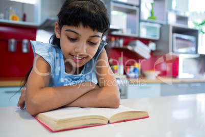 Girl reading novel with arms crossed in kitchen