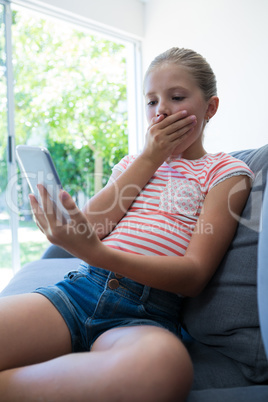 Girl with hands covering mouth holding smartphone