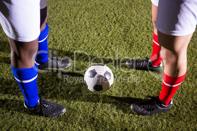 Low section of players standing by soccer ball