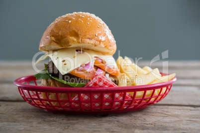 Cheeseburger and French fries in basket against wall