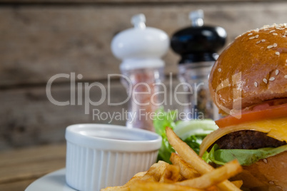 Burger, french fries, sauce in plate on wooden table