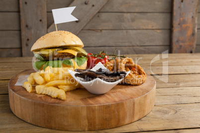 Hamburger, onion ring and french fries on chopping board