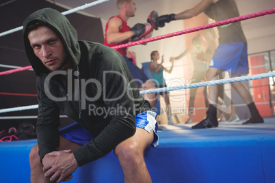 Portrait of young male boxer sitting on boxing ring at fitness studio
