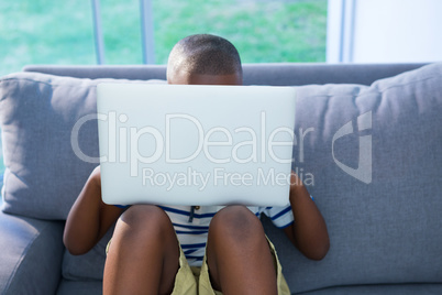 Boy sitting on sofa while using laptop against window at home