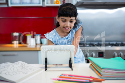Smiling girl using digital tablet amidst colored pencils and books