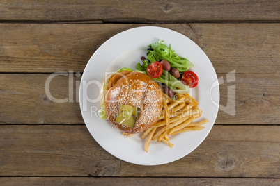 Hamburger, french fries and salad in plate on wooden table