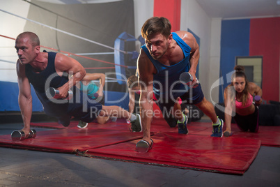 Young athletes exercising with dumbbells by boxing ring