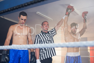 Referee holding hands of winning male boxer by athlete