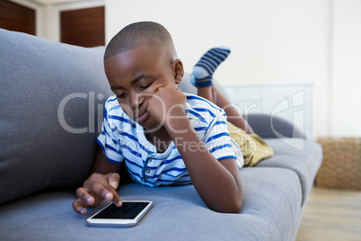 Bored boy lying on sofa while using mobile phone at home
