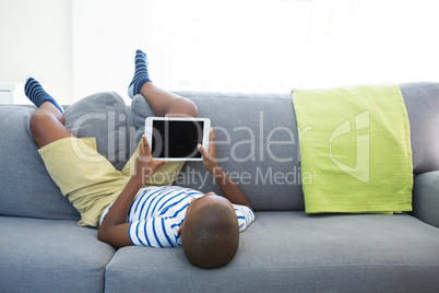 Boy lying on sofa while using digital tablet at home