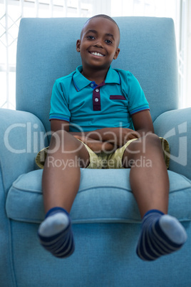 Portrait of smiling boy sitting on blue armchair at home