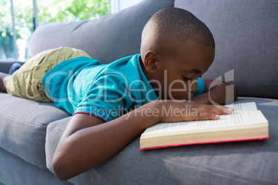 Boy reading novel while lying on sofa at home