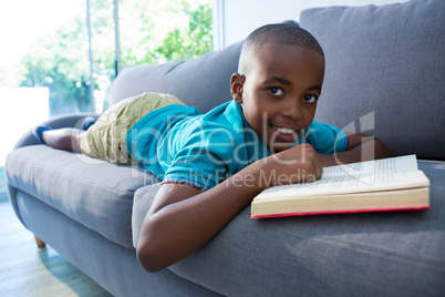 Boy lying on sofa with novel at home