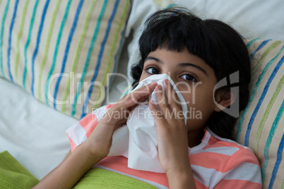 High angle portrait of girl blowing nose on bed