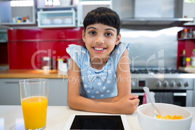Portrait of smiling girl sitting with tablet and breakfast in kitchen