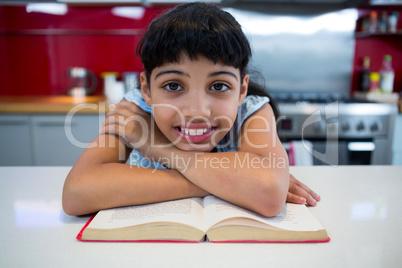 Portrait of smiling girl with arms crossed over novel in kitchen