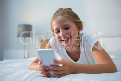 Cheerful girl using smartphone on bed