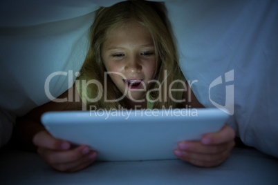 Happy girl using tablet computer with blanket on head