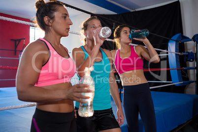 Exhausted young athletes drinking water by boxing ring