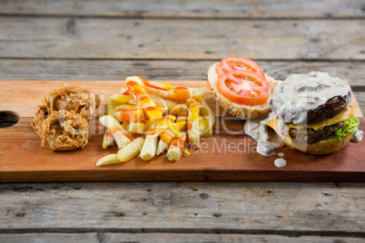 French fries with sauce by onion rings and burger on cutting board