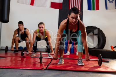 Portrait of female athlete lifting barbell with friends