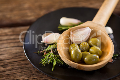 Green olives, rosemary and wooden ladle on table